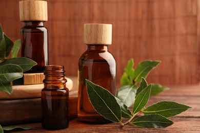 Photo of Bottles of bay essential oil and fresh leaves on wooden table