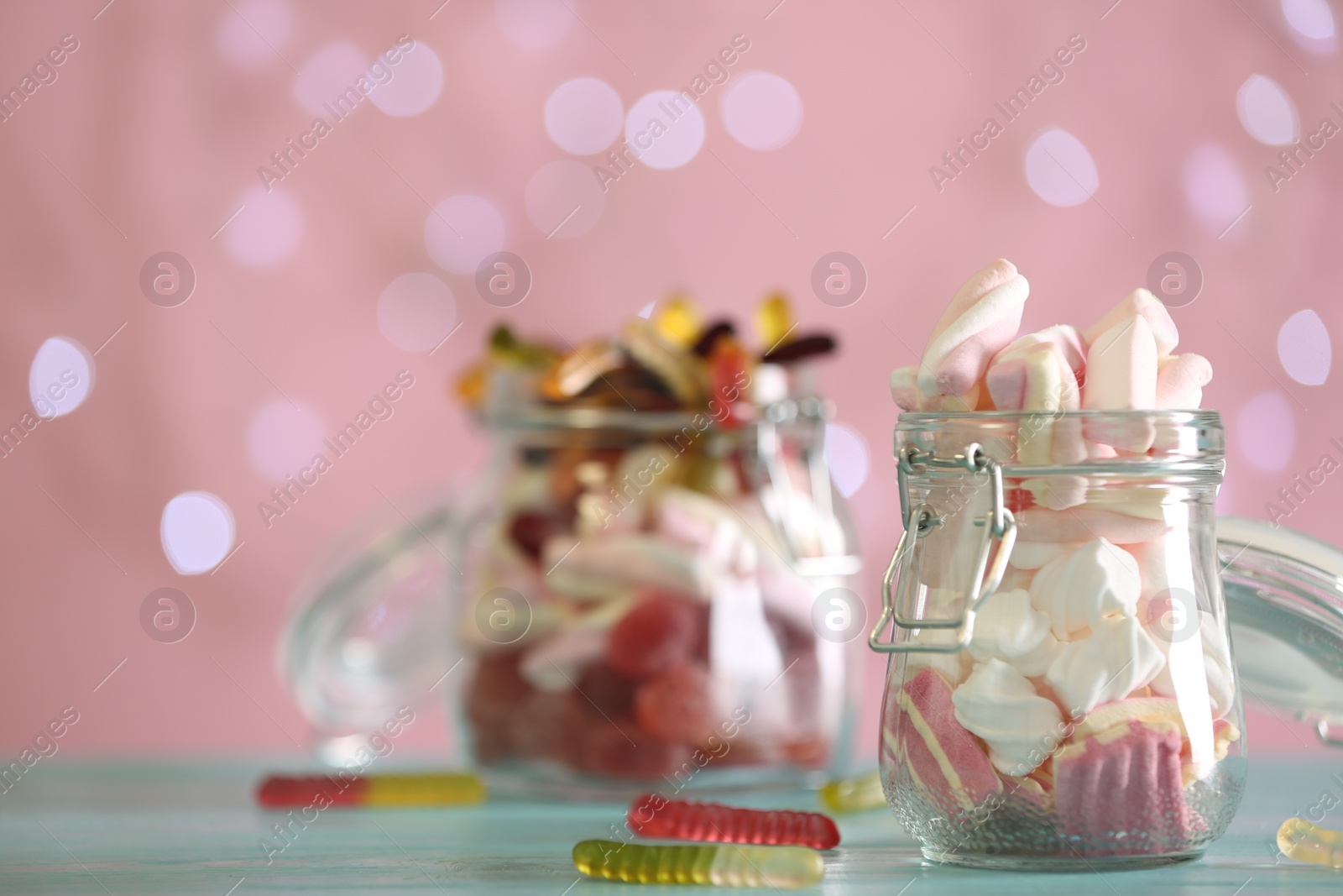 Photo of Delicious marshmallows in jar on table against blurred background, closeup. Space for text