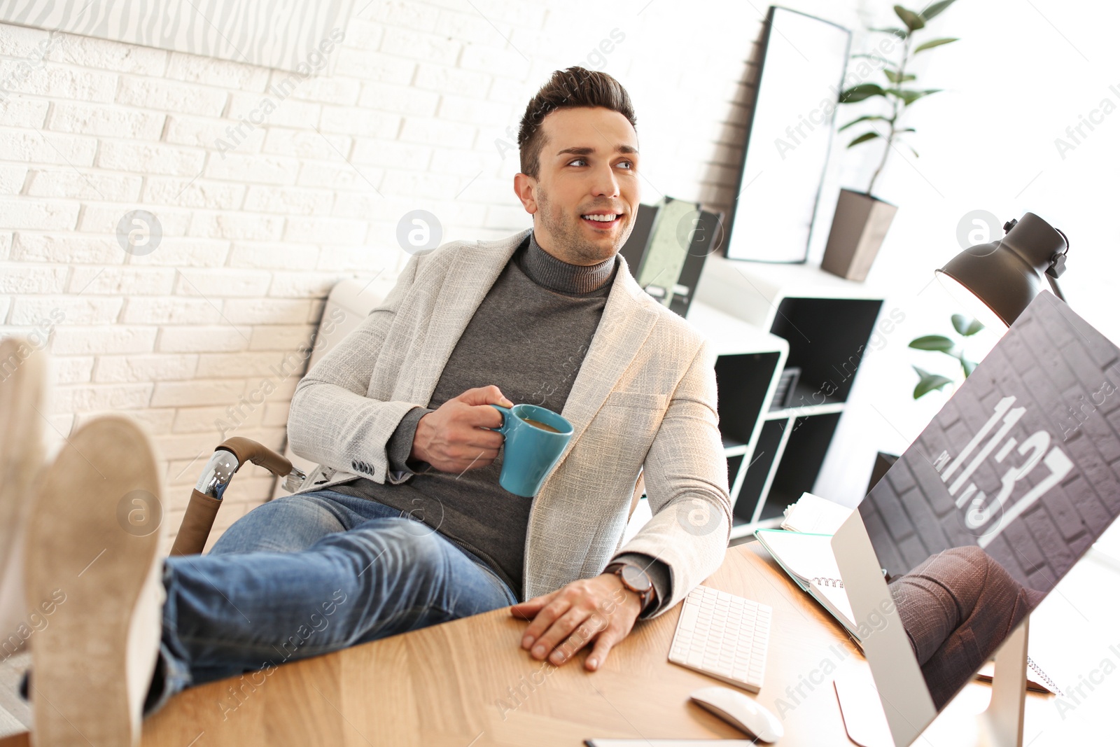 Photo of Young man with cup of drink relaxing at table in office during break