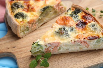 Photo of Pieces of delicious homemade quiche with salmon and broccoli on wooden board, closeup