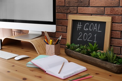 Photo of Blackboard with hashtag Goal 2021 near computer monitor on wooden desk in office