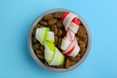 Dry dog food and treats (knotted chew bones) on light blue background, top view