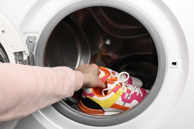 Photo of Woman putting stylish sneakers into washing machine, closeup