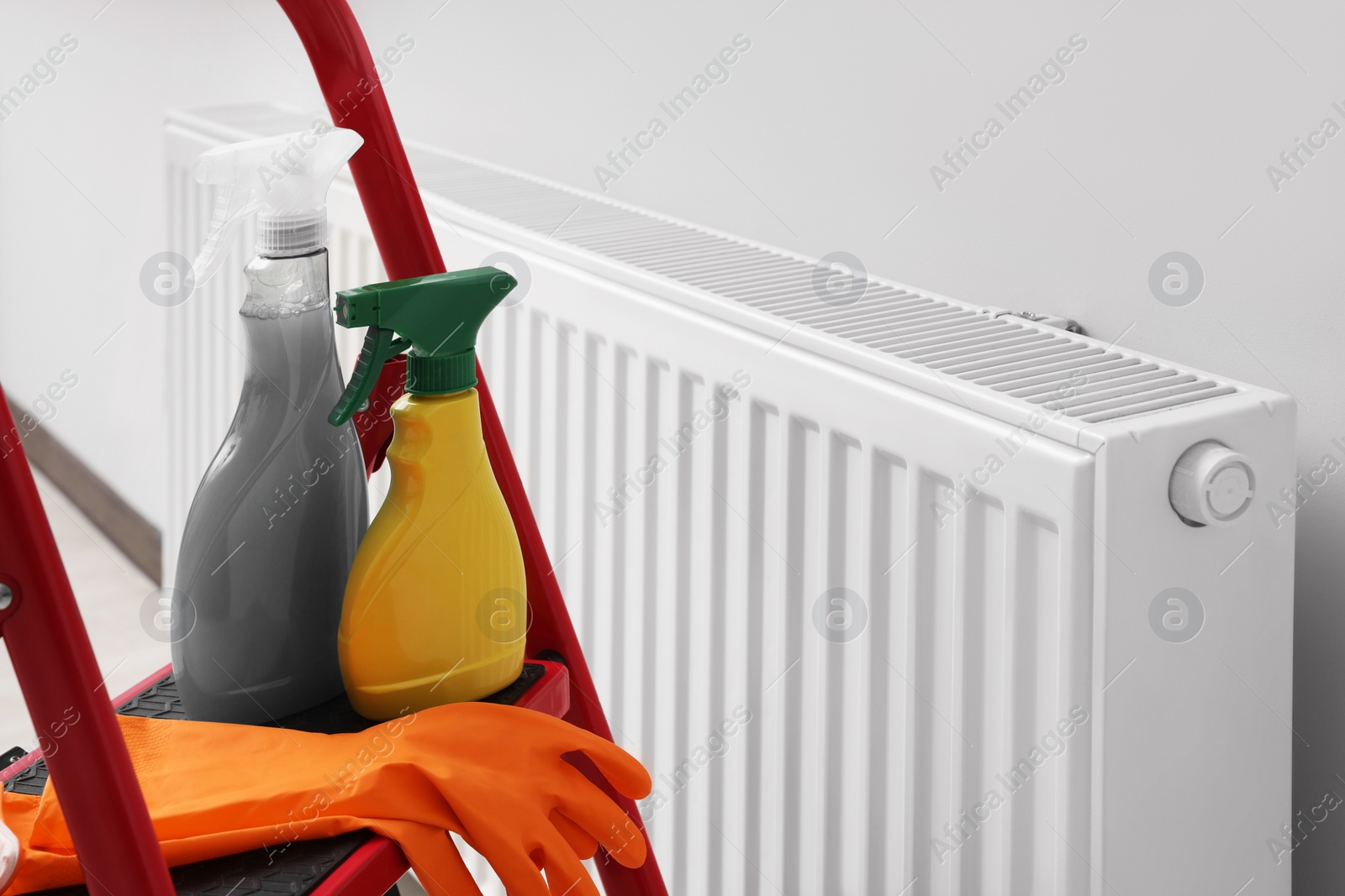 Photo of Ladder with cleaning supplies near modern radiator in room