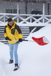 Photo of Man cleaning snow with shovel near house