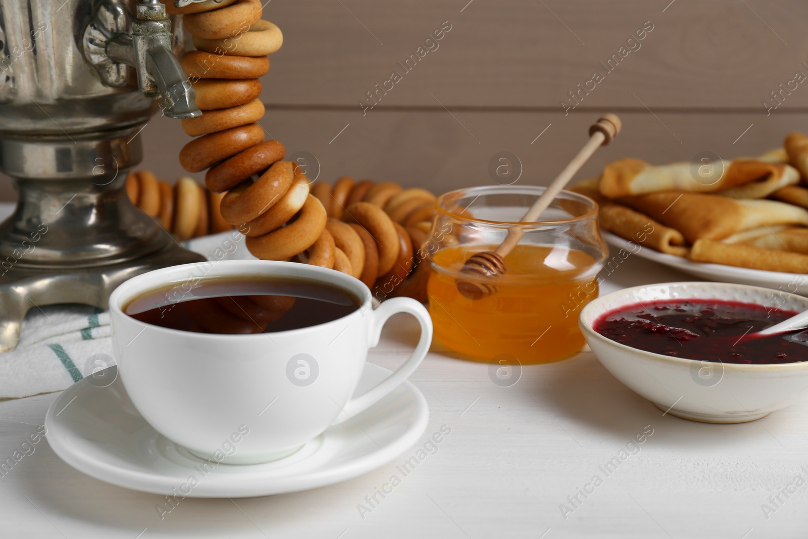 Photo of Metal samovar with cup of tea and treats on white wooden table