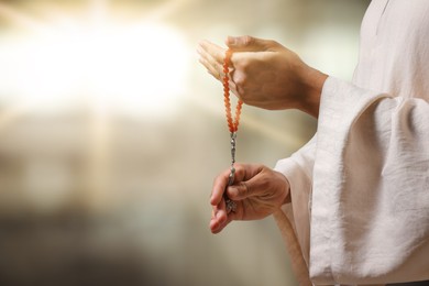 Image of Muslim man with misbaha praying on blurred background, closeup. Space for text
