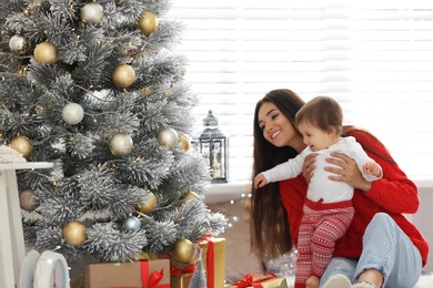 Mother and her cute baby near Christmas tree at home