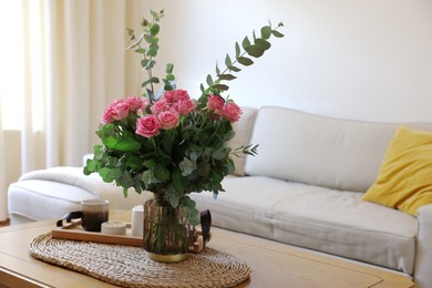 Beautiful bouquet of roses and eucalyptus branches in vase near candles on table at home. Space for text