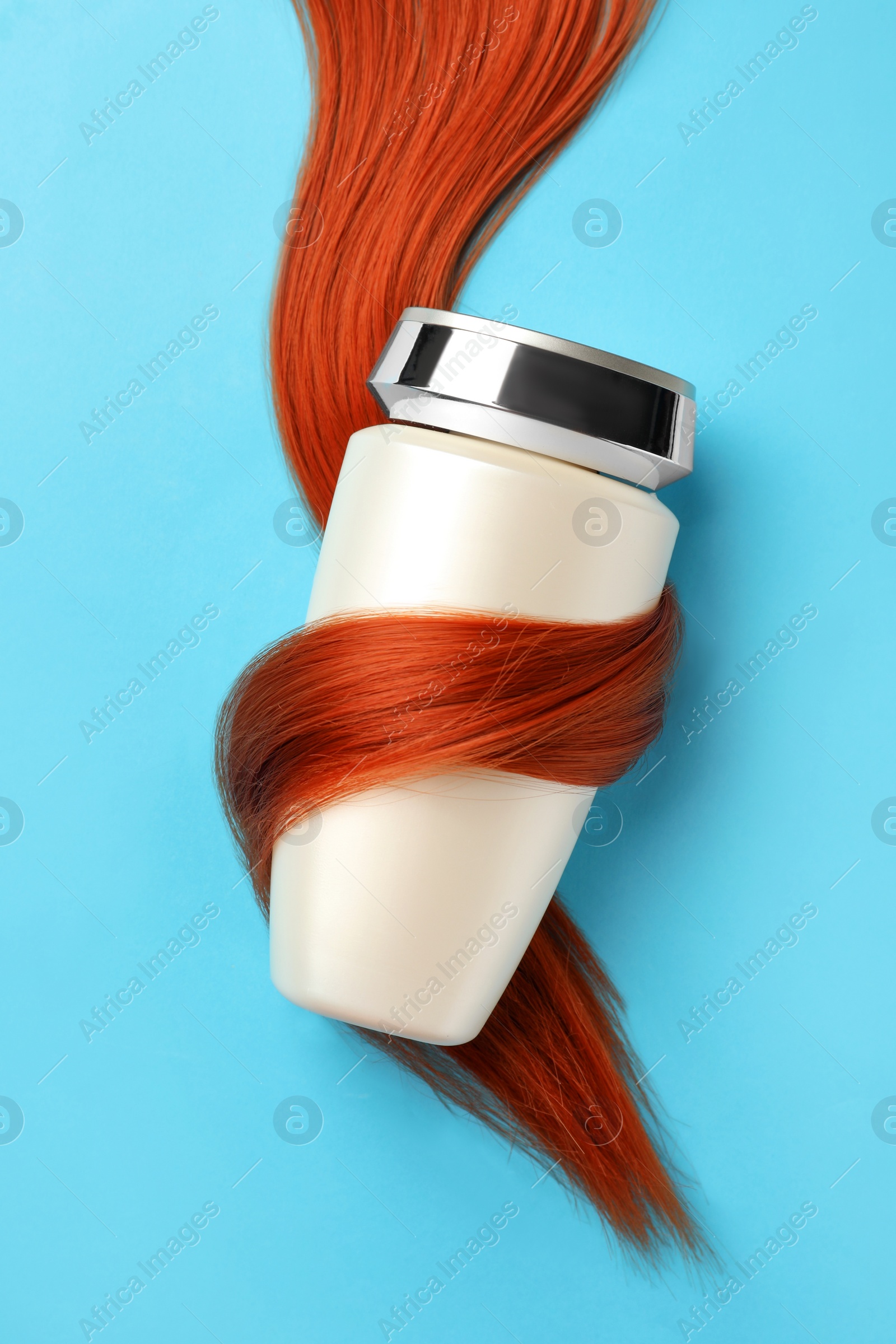 Photo of Bottle wrapped in lock of hair on light blue background, top view. Natural cosmetic product