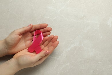 Photo of Breast cancer awareness. Woman with pink ribbon at light grey table, top view. Space for text