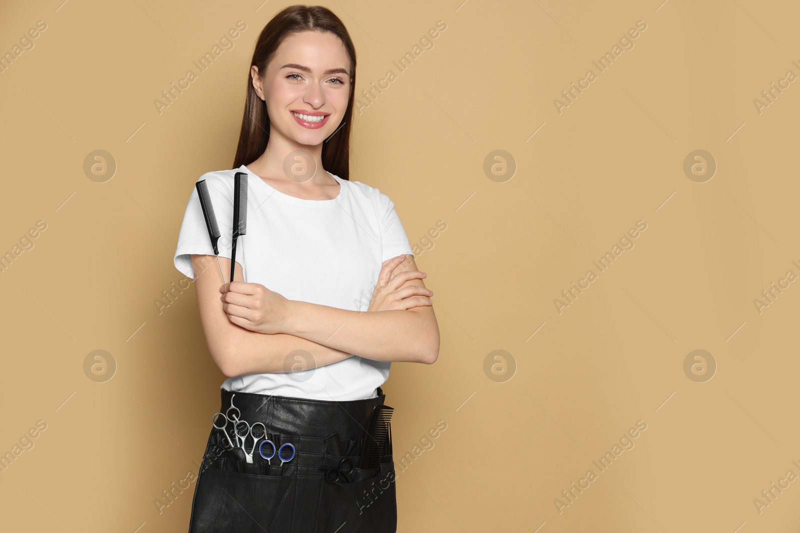 Photo of Portrait of happy hairdresser with combs on beige background. Space for text