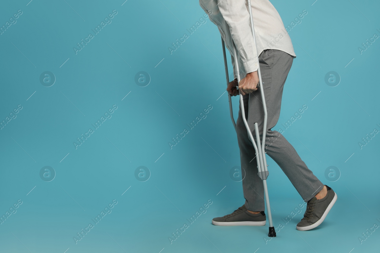 Photo of Man with crutches on light blue background, closeup. Space for text