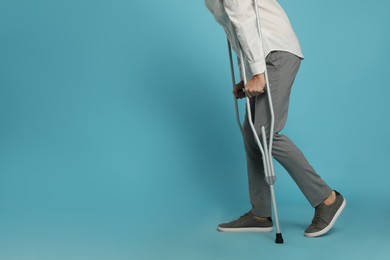 Photo of Man with crutches on light blue background, closeup. Space for text