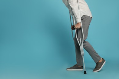 Man with crutches on light blue background, closeup. Space for text