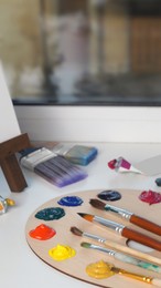 Photo of Artist's palette with samples of colorful paints and brushes on white table