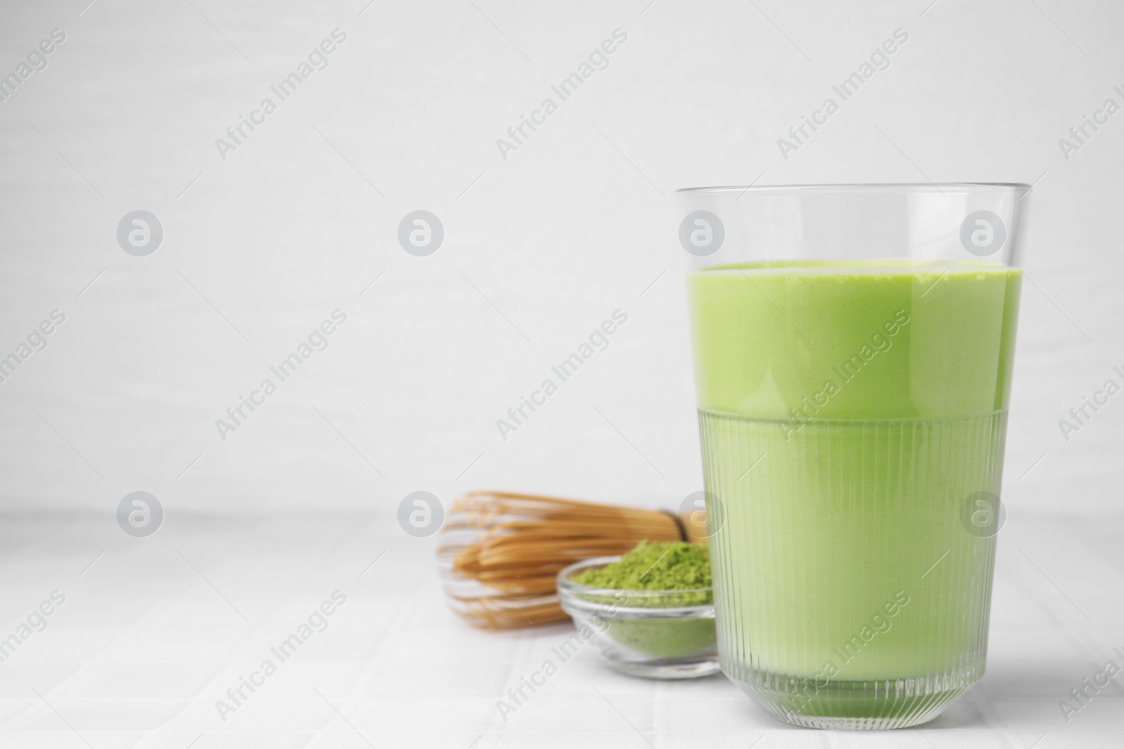 Photo of Glass of tasty matcha smoothie, powder and bamboo whisk on white tiled table, space for text