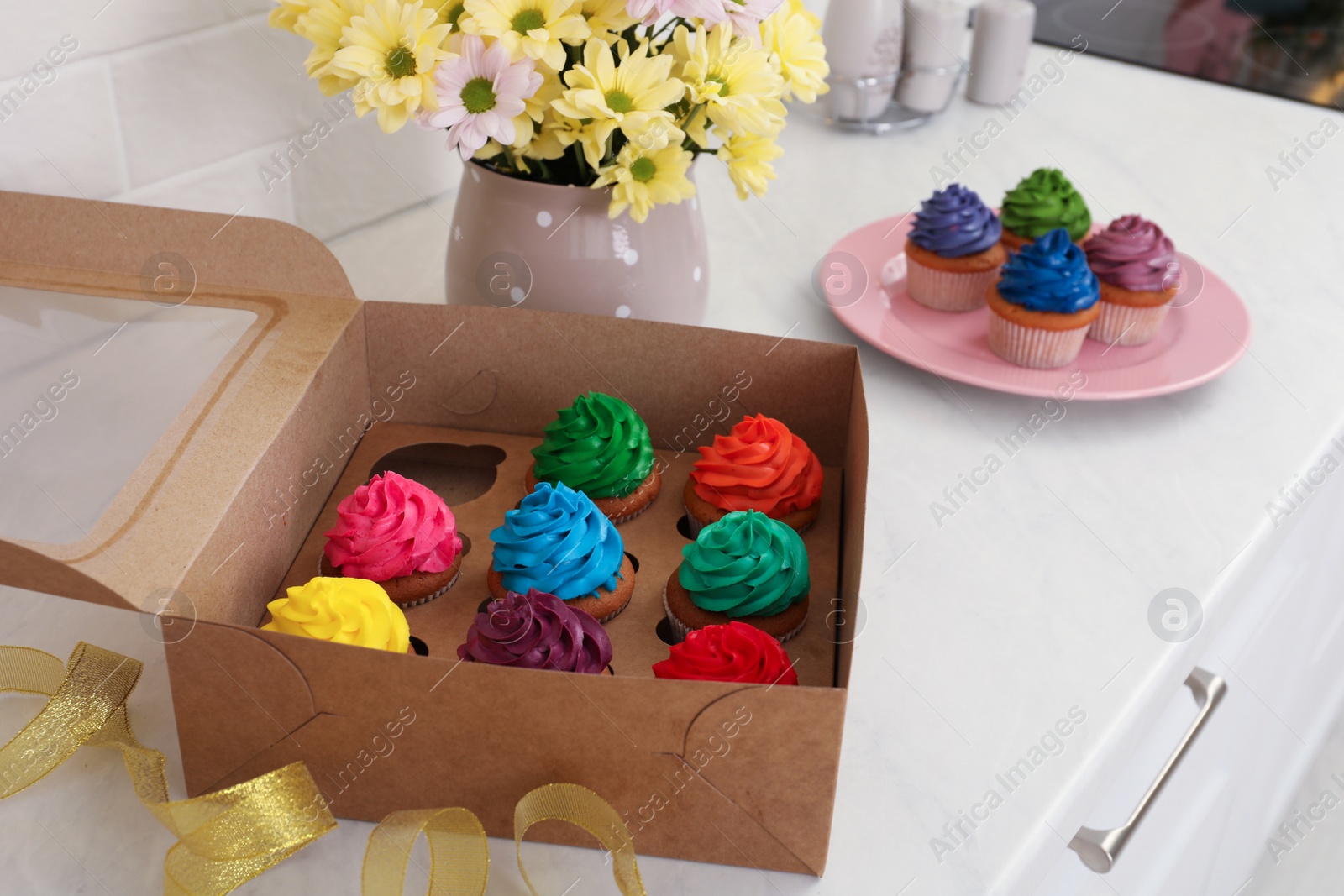 Photo of Delicious colorful cupcakes and beautiful flowers on white table indoors