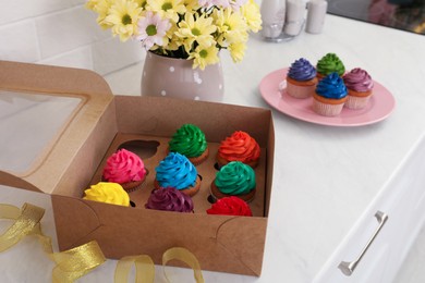 Delicious colorful cupcakes and beautiful flowers on white table indoors