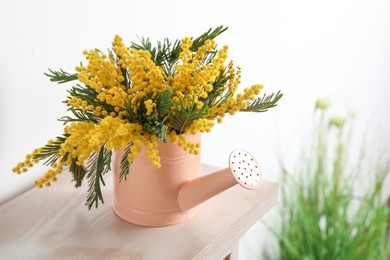 Beautiful mimosa flowers in watering can on wooden table