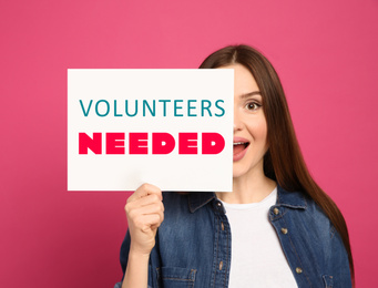 Image of Emotional woman holding paper with text VOLUNTEERS NEEDED on pink background