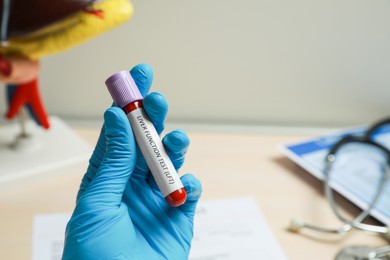 Laboratory worker holding tube with blood sample and label Liver Function Test over table, closeup