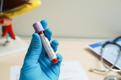 Photo of Laboratory worker holding tube with blood sample and label Liver Function Test over table, closeup