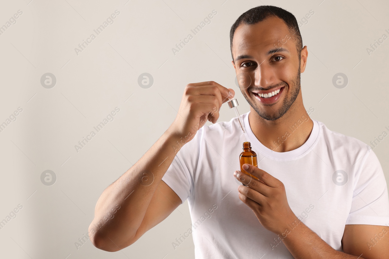 Photo of Handsome man with cosmetic serum in hands on light grey background, space for text