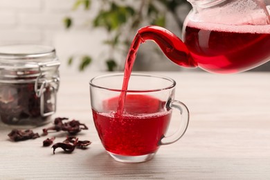 Pouring delicious hibiscus tea into cup on white wooden table, closeup