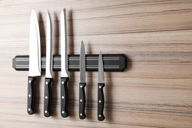 Photo of Magnetic holder with set of knives on wooden background. Space for text