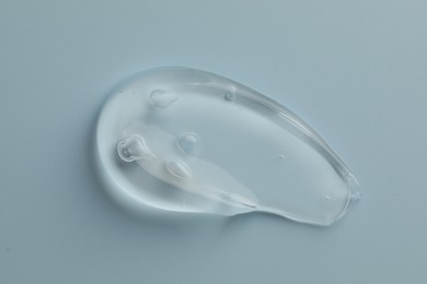 Photo of Smear of clear cosmetic gel on light blue background, top view