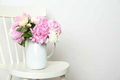 Photo of Beautiful peonies in jug on white chair. Space for text