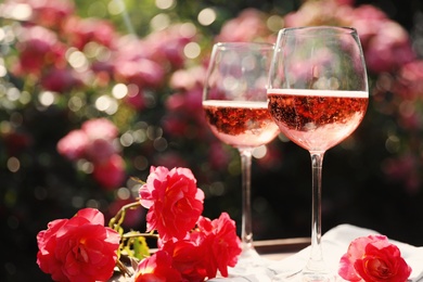 Glasses of rose wine on table in blooming garden, space for text