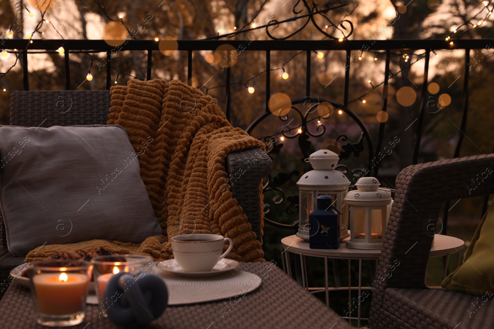 Photo of Beautiful view of garden furniture with pillow, soft blanket and burning candles at balcony