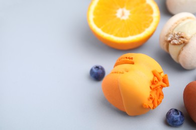 Delicious macaron, orange and berries on light blue table, closeup. Space for text