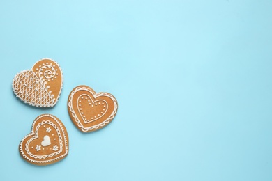 Photo of Gingerbread hearts decorated with icing on light blue background, flat lay. Space for text