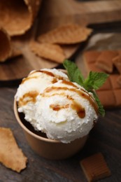 Photo of Scoops of tasty ice cream with caramel sauce, mint leaves and candies on wooden table, closeup