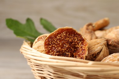 Wicker basket with tasty dried figs and green leaf on table, closeup