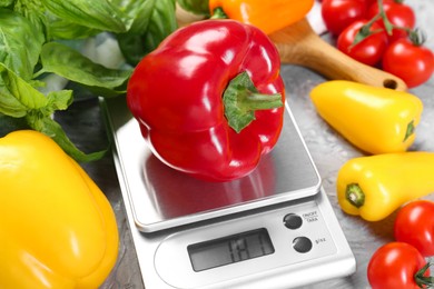 Photo of Kitchen scale with bell pepper among basil and tomatoes on grey textured table, closeup