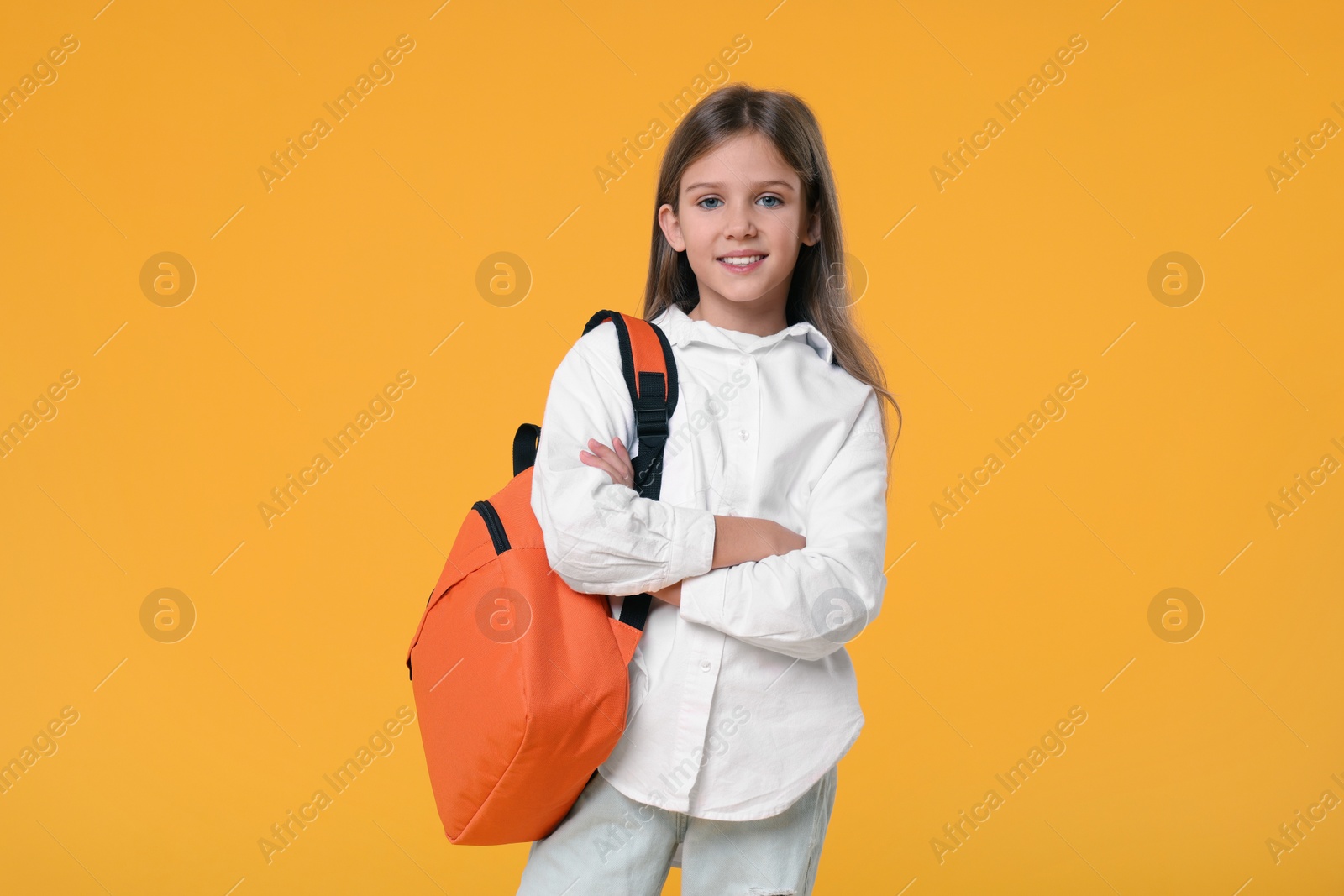 Photo of Happy schoolgirl with backpack on orange background