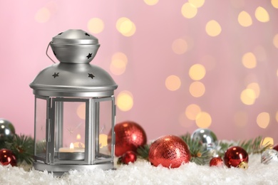Christmas lantern with burning candle and festive decor on snow against blurred lights