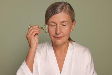 Photo of Woman massaging her face with jade roller on green background