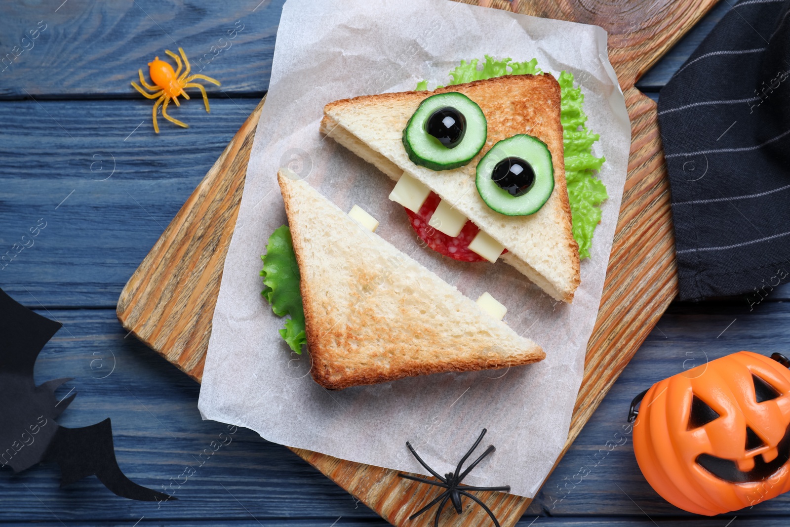 Photo of Cute monster sandwich served on blue wooden table, flat lay. Halloween party food