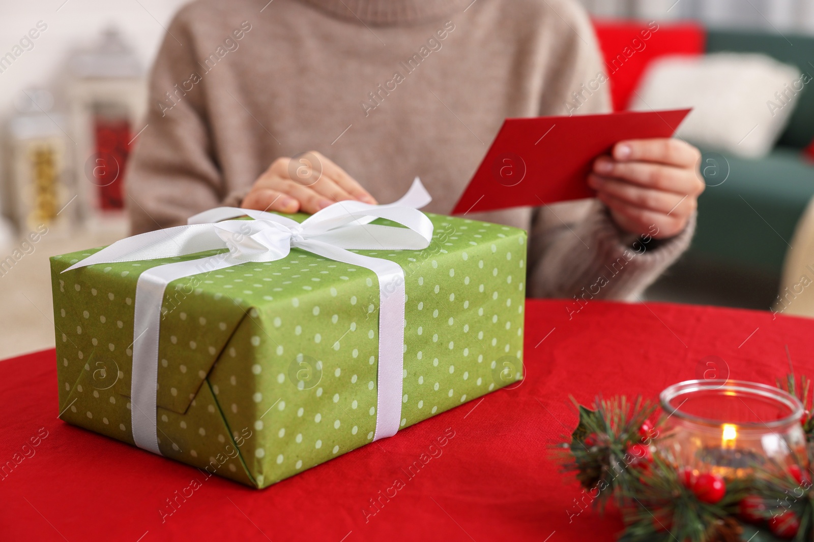 Photo of Woman with Christmas gift reading greeting card at table indoors, selective focus