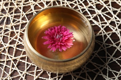 Tibetan singing bowl with water and beautiful flower on wooden table