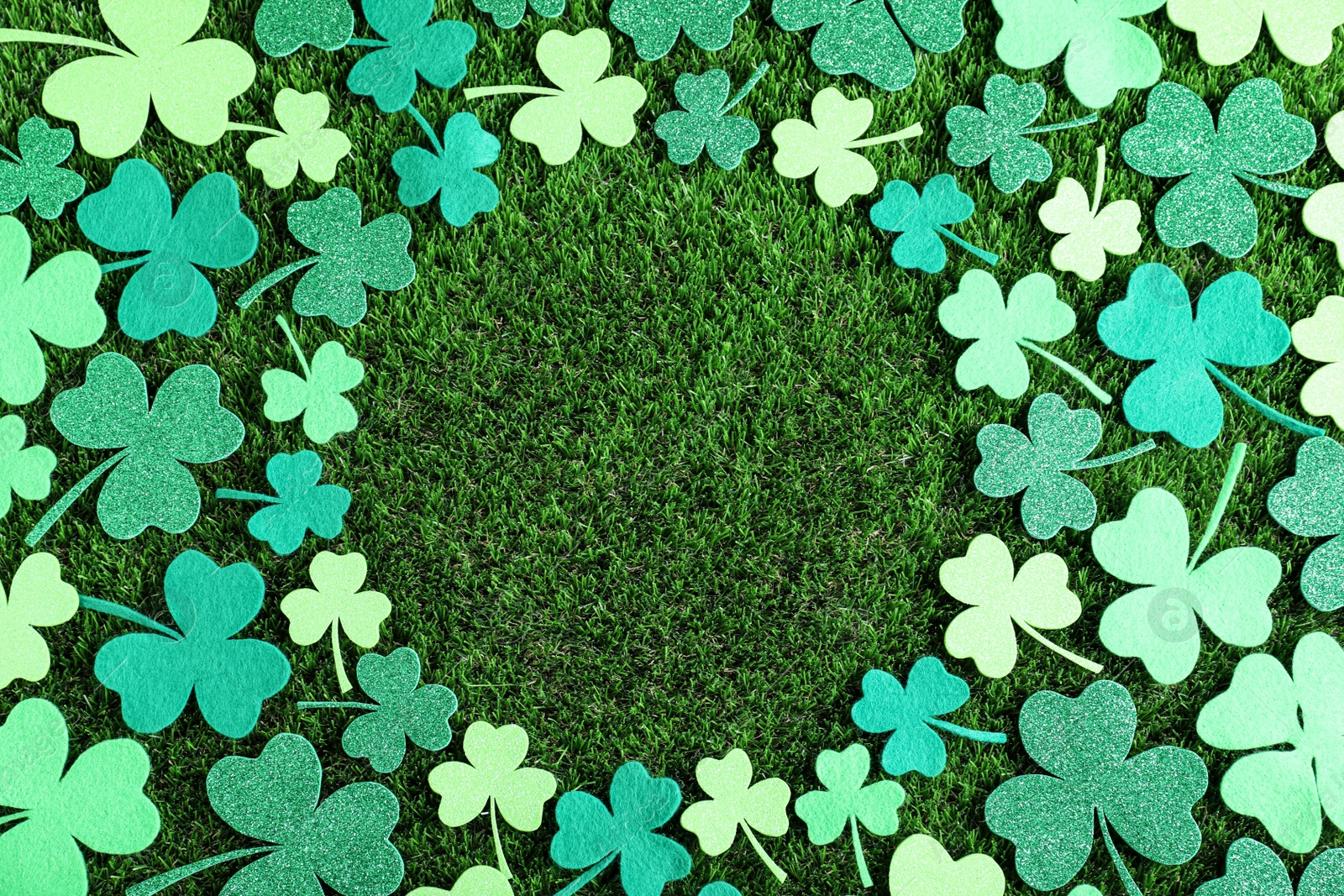 Photo of Frame made of clover leaves on green grass, flat lay with space for text. St. Patrick's Day celebration