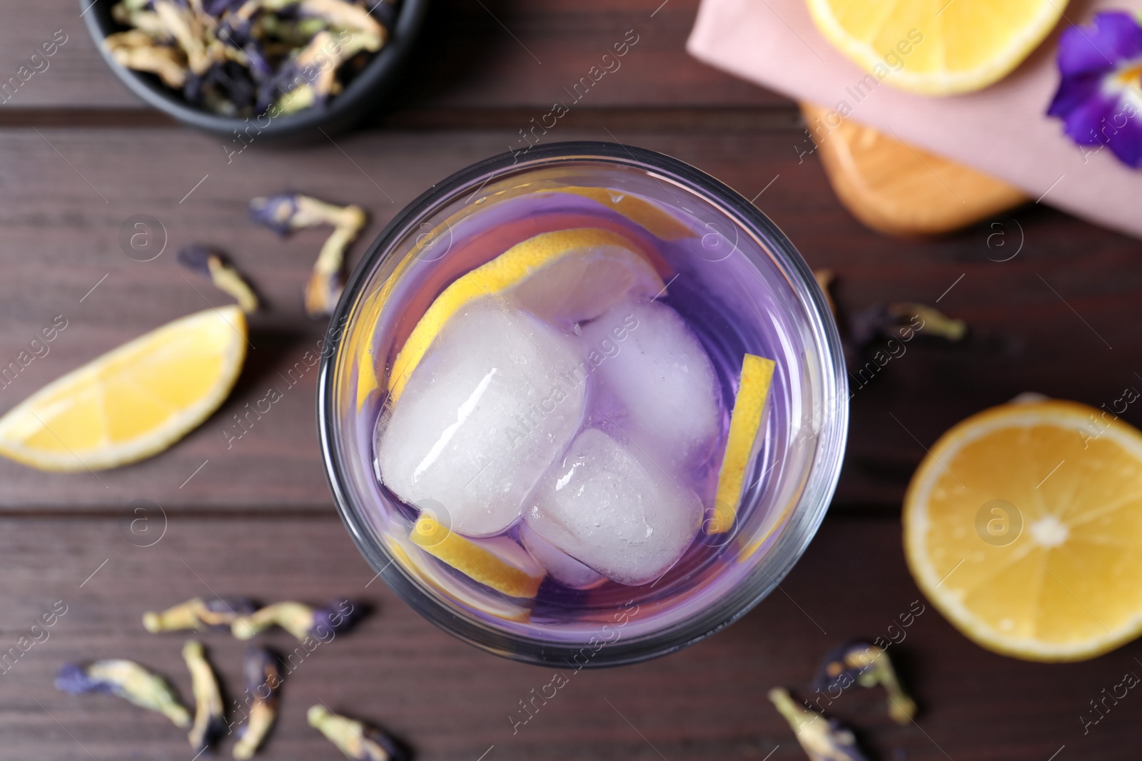 Photo of Organic blue Anchan with lemon in glass on wooden table, flat lay. Herbal tea