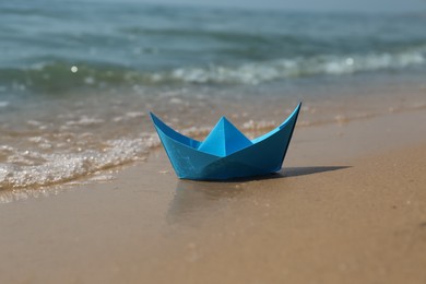 Photo of Blue paper boat on sandy beach near sea
