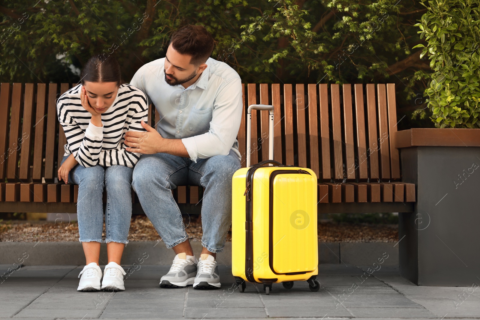 Photo of Long-distance relationship. Man calming his sad girlfriend on bench and suitcase outdoors