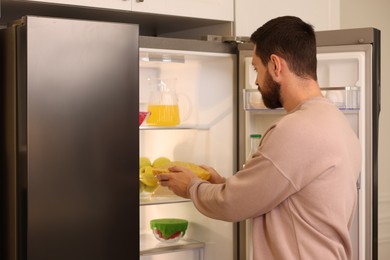 Man putting bowl covered with beeswax food wrap into refrigerator indoors